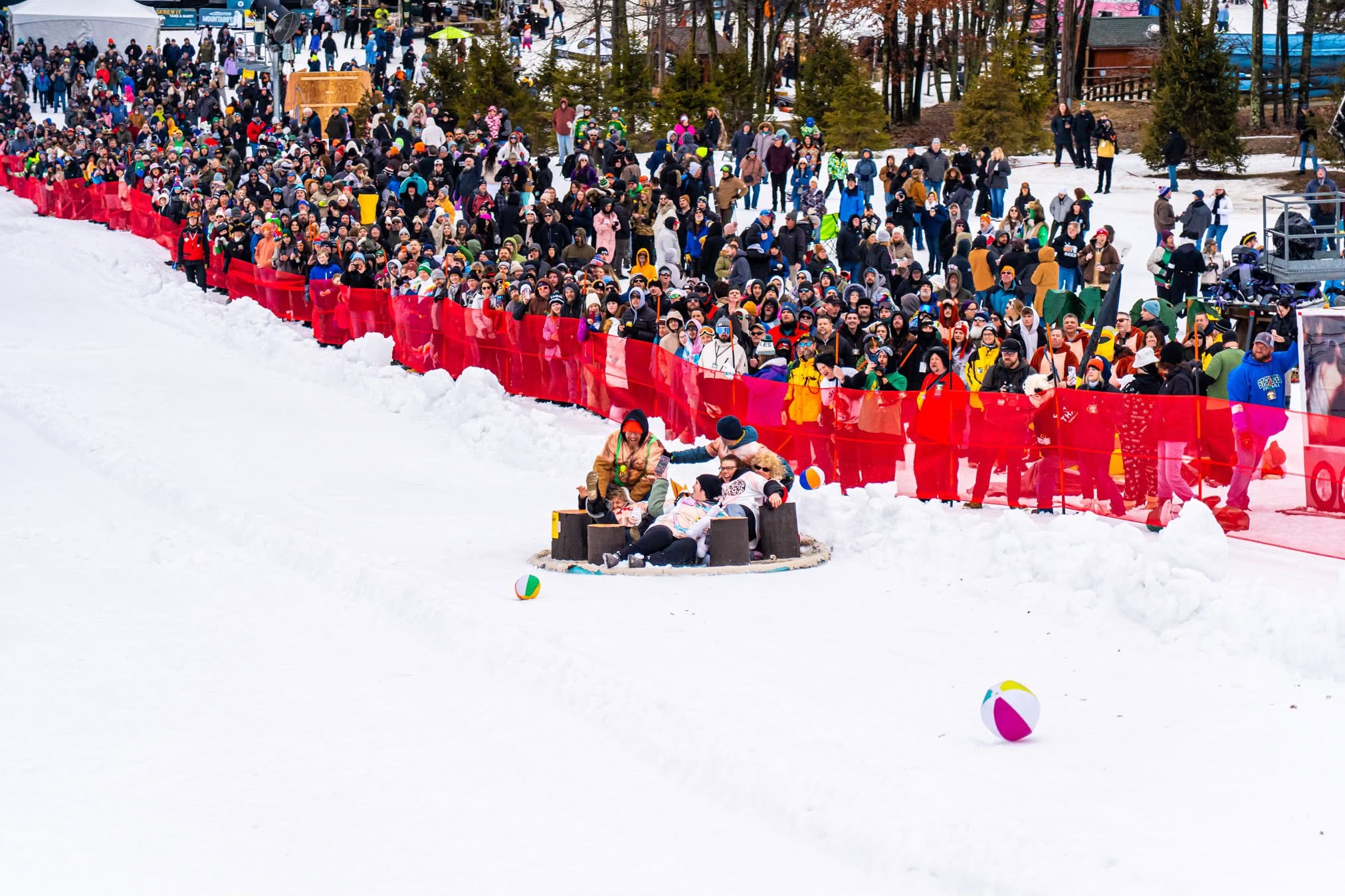 A Cardboard Classic team racing downhill past spectators on the snow